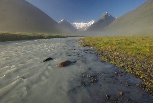 The mountain river in the mountains. Current through the gorge the river. Stones and rocky land near the river. Beautiful mountain landscape.