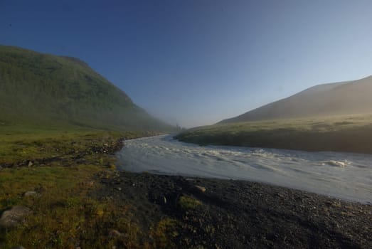 The mountain river in the mountains. Current through the gorge the river. Stones and rocky land near the river. Beautiful mountain landscape.