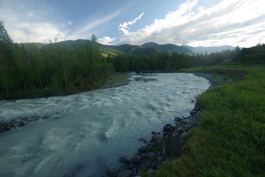 The mountain river in the mountains. Current through the gorge the river. Stones and rocky land near the river. Beautiful mountain landscape.