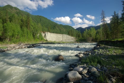 The mountain river in the mountains. Current through the gorge the river. Stones and rocky land near the river. Beautiful mountain landscape.