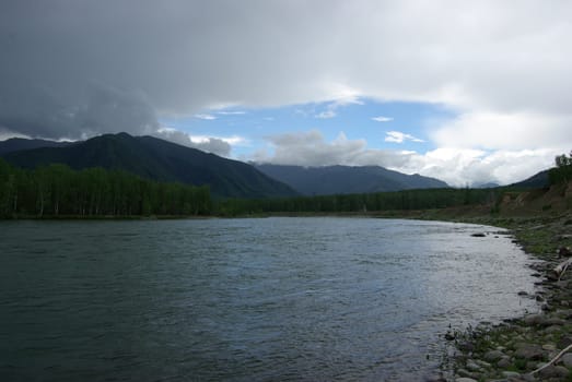 The mountain river in the mountains. Current through the gorge the river. Stones and rocky land near the river. Beautiful mountain landscape.