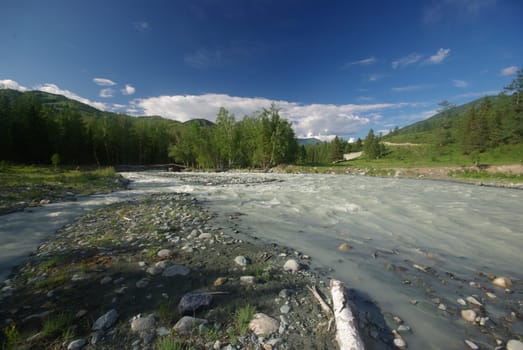 The mountain river in the mountains. Current through the gorge the river. Stones and rocky land near the river. Beautiful mountain landscape.