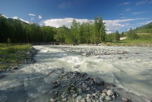 The mountain river in the mountains. Current through the gorge the river. Stones and rocky land near the river. Beautiful mountain landscape.
