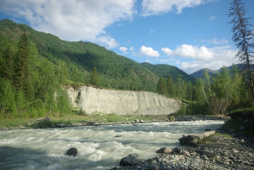 The mountain river in the mountains. Current through the gorge the river. Stones and rocky land near the river. Beautiful mountain landscape.