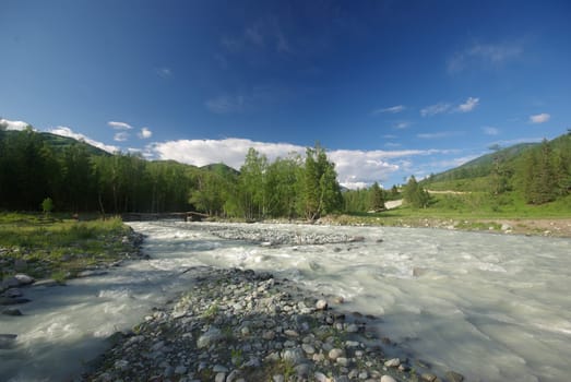 The mountain river in the mountains. Current through the gorge the river. Stones and rocky land near the river. Beautiful mountain landscape.