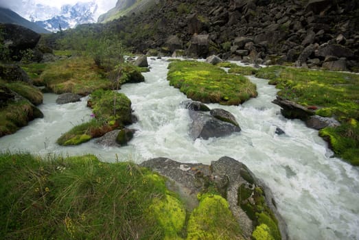 The mountain river in the mountains. Current through the gorge the river. Stones and rocky land near the river. Beautiful mountain landscape.
