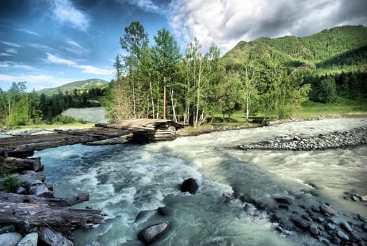 The mountain river in the mountains. Current through the gorge the river. Stones and rocky land near the river. Beautiful mountain landscape.