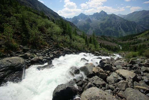 The mountain river in the mountains. Current through the gorge the river. Stones and rocky land near the river. Beautiful mountain landscape.