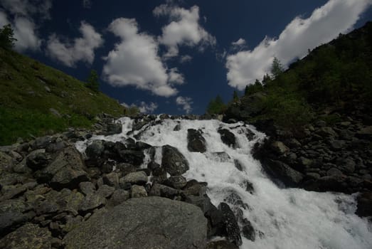 The mountain river in the mountains. Current through the gorge the river. Stones and rocky land near the river. Beautiful mountain landscape.
