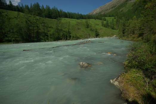 The mountain river in the mountains. Current through the gorge the river. Stones and rocky land near the river. Beautiful mountain landscape.
