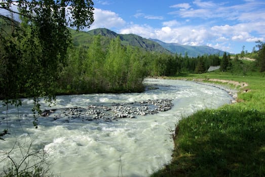 The mountain river in the mountains. Current through the gorge the river. Stones and rocky land near the river. Beautiful mountain landscape.