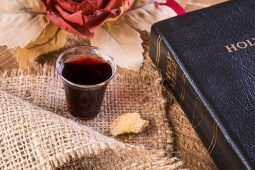 Taking Communion. Cup of glass with red wine, bread and Holy Bible on wooden table close-up. Focus on glass.
