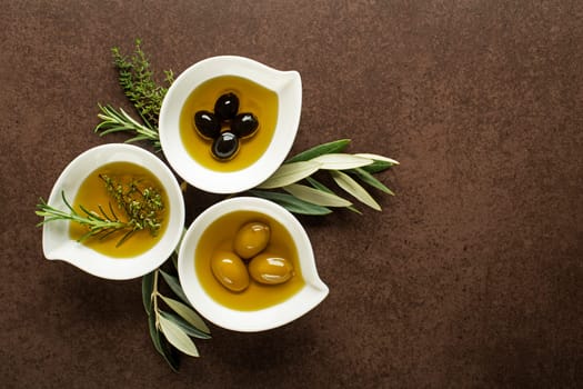 Olive oil with fresh herbs on brown background