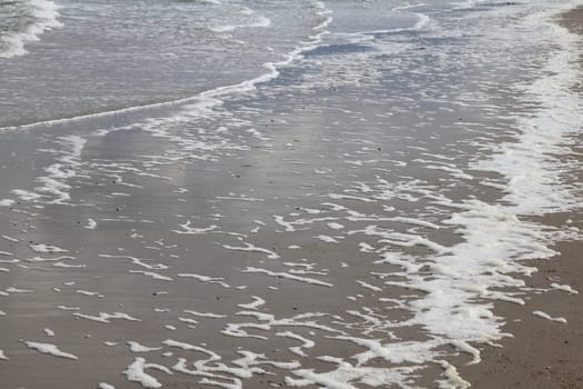 Waves with white foam crowns flood the sandy beach.