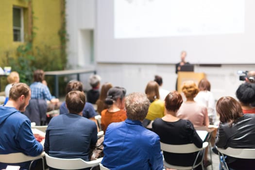 Business and entrepreneurship symposium. Speaker giving a talk at business meeting. Audience in the conference hall. Rear view of unrecognized participant in audience.