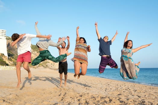 Group of happy teenage friends jumping at the beach