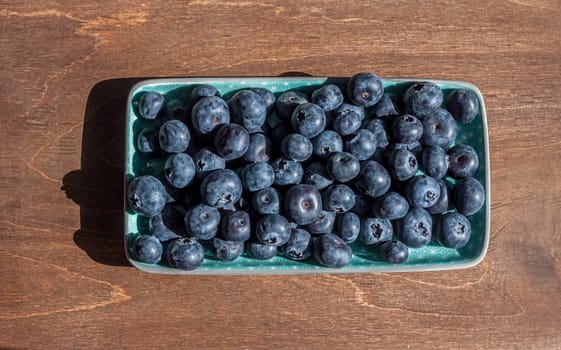 fresh big delicious blueberries in rectangular green plate wooden background