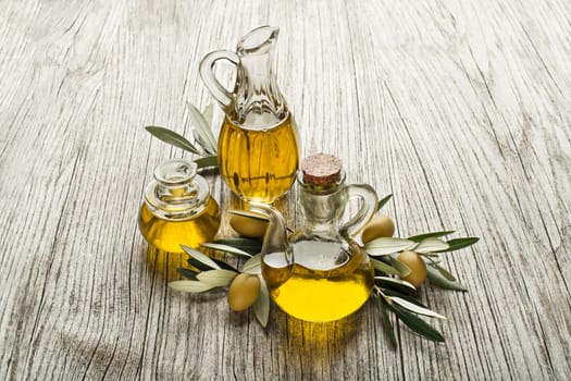 Olive oil in bottles with branch on the wooden background
