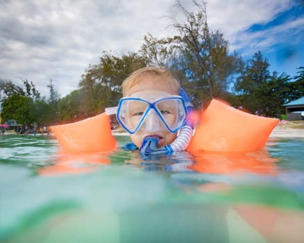 Boy with armbands, mask and snorkel plays in a sea