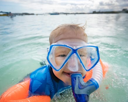 Boy with armbands, mask and snorkel plays in a sea
