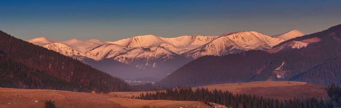 Rolling green hills and snow covered mountain peaks panorama