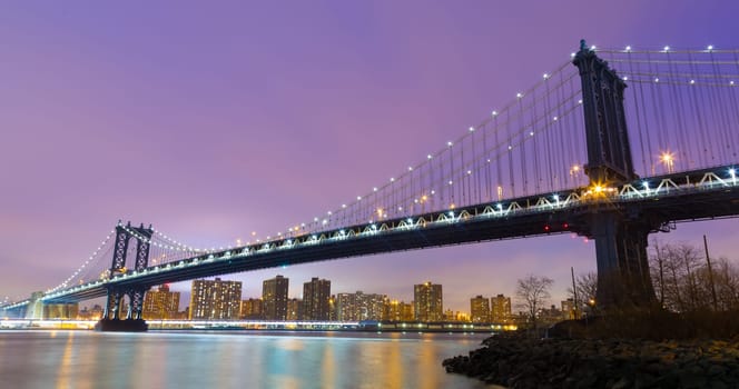 Manhattan bridge and New York City downtown skyline at dusk with skyscrapers illuminated over East River panorama. Copy space.