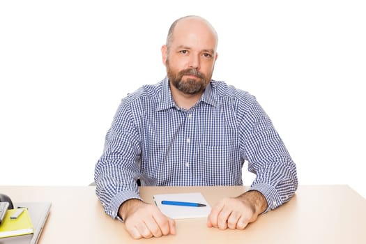 A man with a beard at his desk with a notepad and ballpoint pen in front of a white background