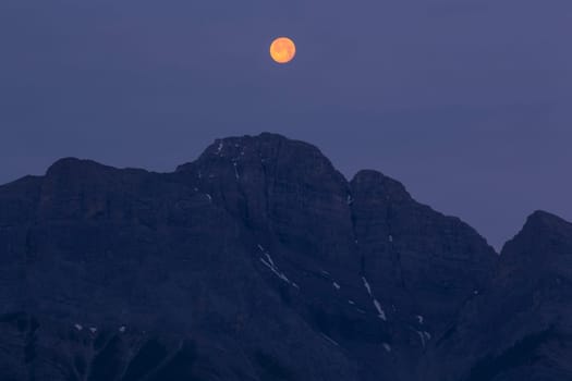 Full moon in early morning sunlight hanging above a mountain range in the Canadian Rocky Mountains, Alberta, Canada