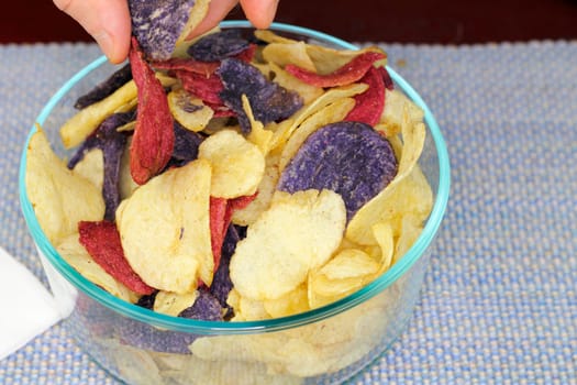 Adult male fingers picking up one of each of three colors of potato chips. Yellow, red and purple potato chips chosen by fingers of an adult male.