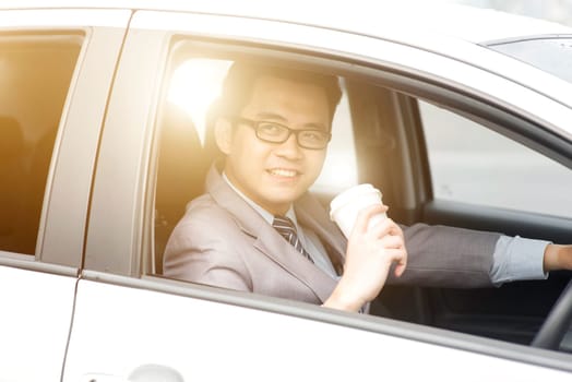 Asian business man driving a car and holding paper cup of coffee in morning with beautiful sunlight.