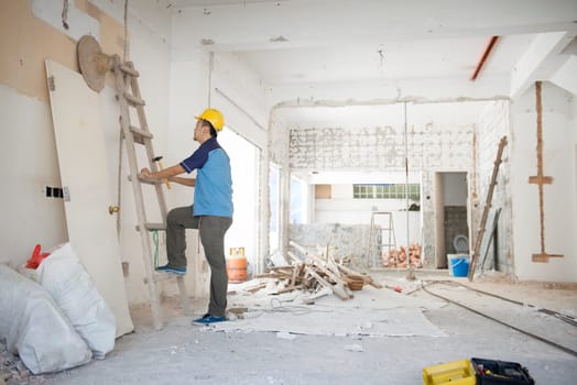 Asian construction worker with hardhat climbing up ladder at site, house renovation.