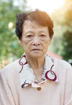 Portrait of upset Asian senior adult woman at outdoor garden park in the morning.