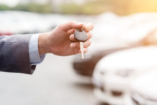 Close up hand holding car key, many automobile at the background.