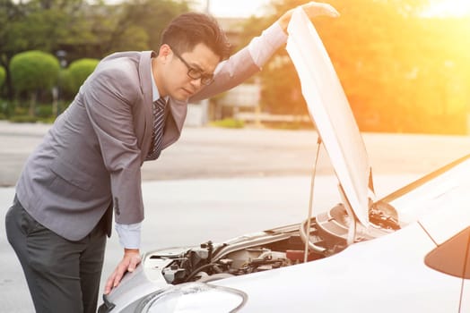 Young Asian business man looking under the hood of breakdown car.
