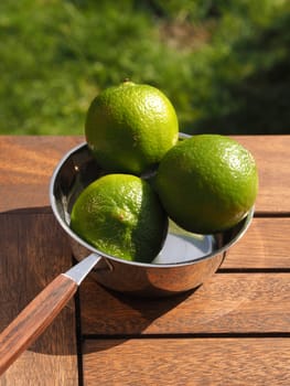 Three fresh organic lime fruits in a steel bowl on a wooden garden table