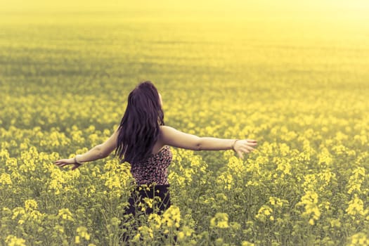 Attractive happy young girl enjoying the warm summer sun and her health in a wide green and yellow meadow. Part of series.