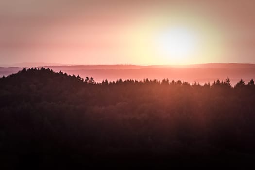 Sunrise or sundown at the horizon of a large forest in Germany in europe. A very idyllic and magical scene with beautiful colors.