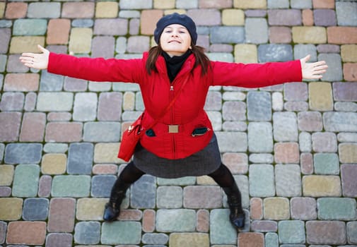 Happy girl. Pretty young smiling woman in a red jacket and beret is standing with arms outstretched and looking up.