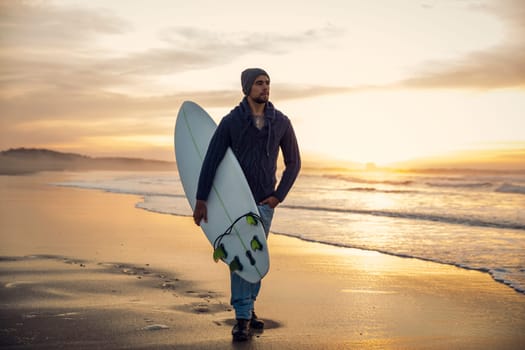 A surfer with his surfboard at the sunset looking to the waves