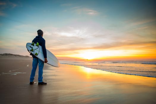 A surfer with his surfboard at the sunset looking to the waves