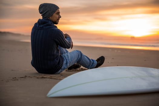 A surfer with his surfboard at the sunset looking to the waves