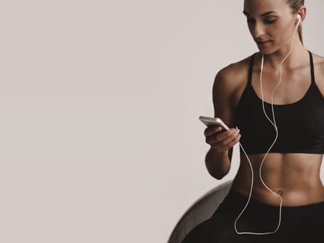 Shot of a beautiful young woman setting the music playlist for the workout.