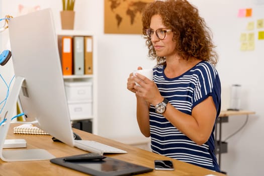 Middle aged woman working on the office and drinking coffee