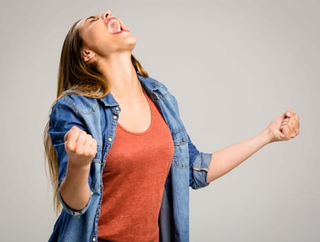 Beautiful happy woman with arms up over a gray background