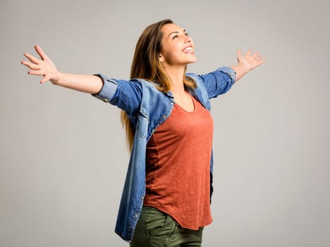 Beautiful happy woman with arms up over a gray background