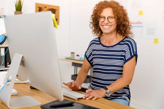 Middle age designer working on a desktop at her office