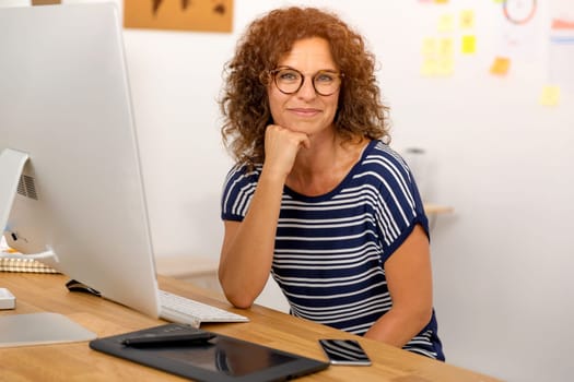 Middle age designer working on a desktop at her office