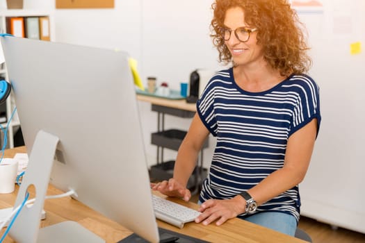 Middle age designer working on a desktop at her office