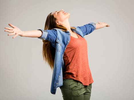 Beautiful happy woman with arms up over a gray background