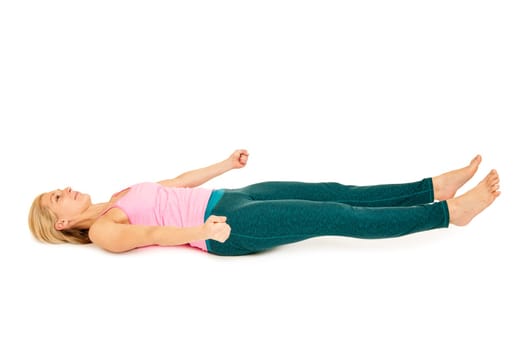 Flat-angled full-body side view of a young woman lying on her back in variation of the yoga position "totenstellung"" (shavasana) on a white background."